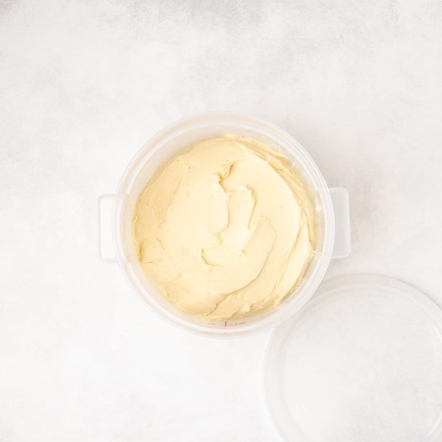 Smooth raw bread dough transferred into a round plastic container with a lid placed beside it.