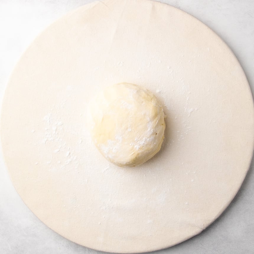 Smooth, raw ball of dough placed on a lightly floured cloth surface.