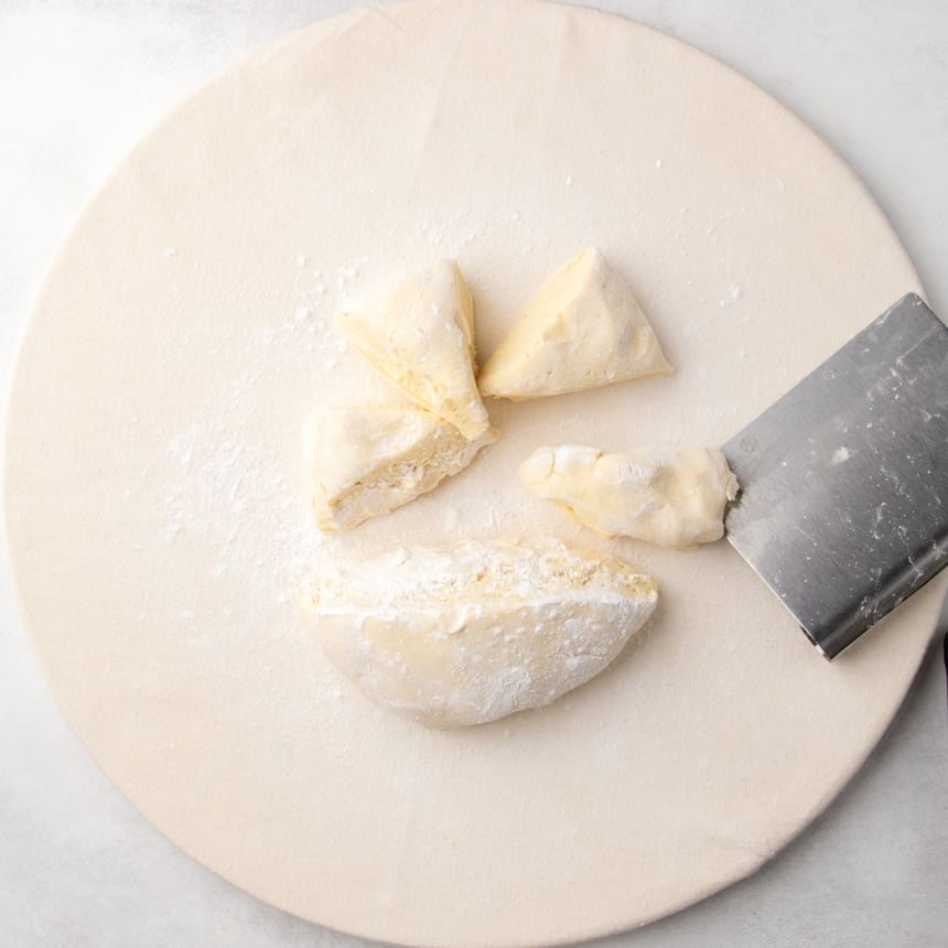 Raw disk of dough cut in half, then cut half into four equal wedges on a floured cloth surface with a bench scraper.