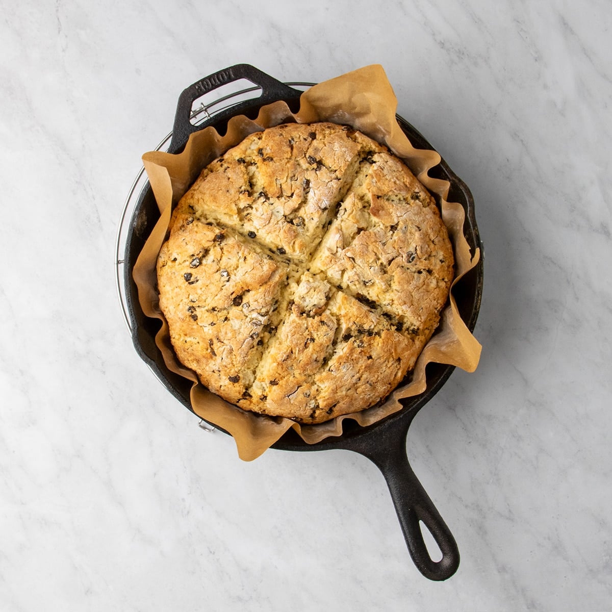 Round baked golden brown loaf of gluten free Irish soda bread with an X on top in a parchment-lined cast iron skillet.