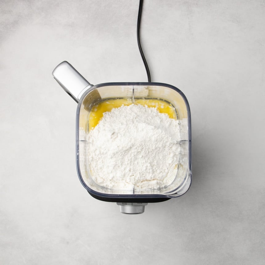 Blender container filled with flour on top of yellow liquid.