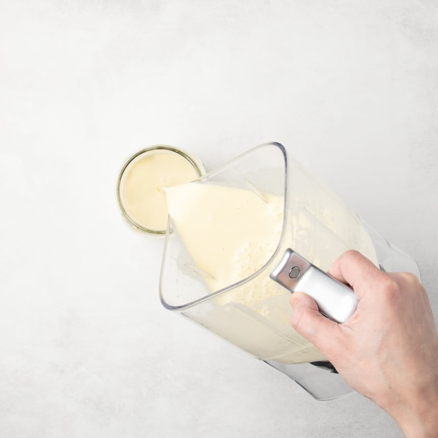 Hand pouring yellow batter from a blender container into a glass jar.