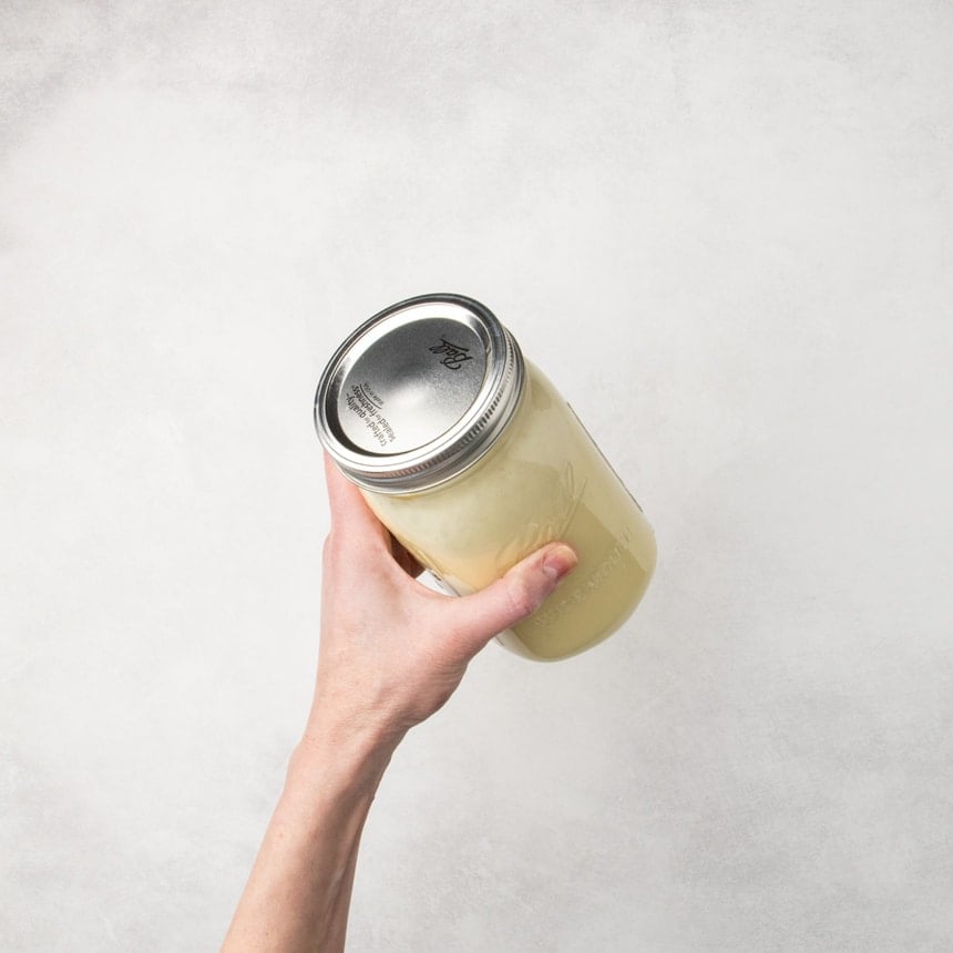 Hand holding a glass jar filled with light yellow liquid batter and sealed with a lid.