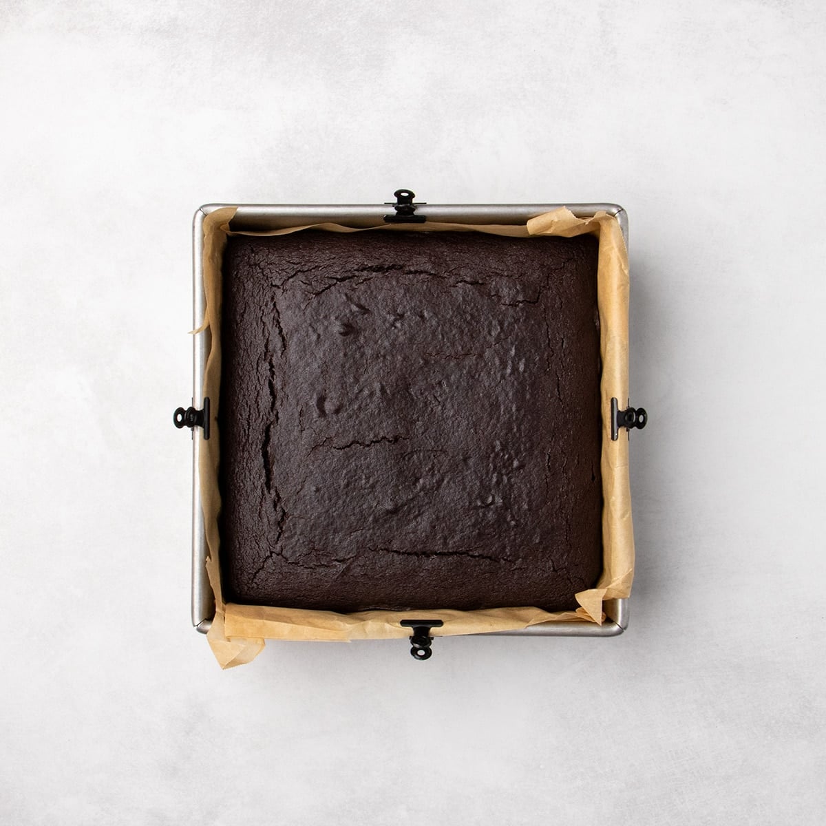 A baked rectangular dairy free gluten free chocolate cake in a parchment-lined pan with a cracked top surface.