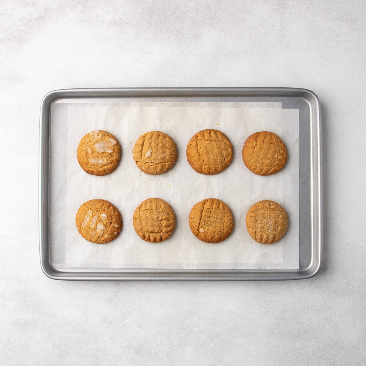 8 round baked gluten free peanut butter cookies with crosshatch fork marks arranged on a parchment-lined baking sheet.