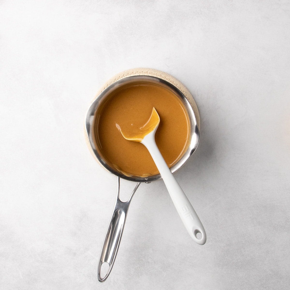 Smooth melted peanut butter mixture in a small metal saucepan with a white silicone spatula resting inside.