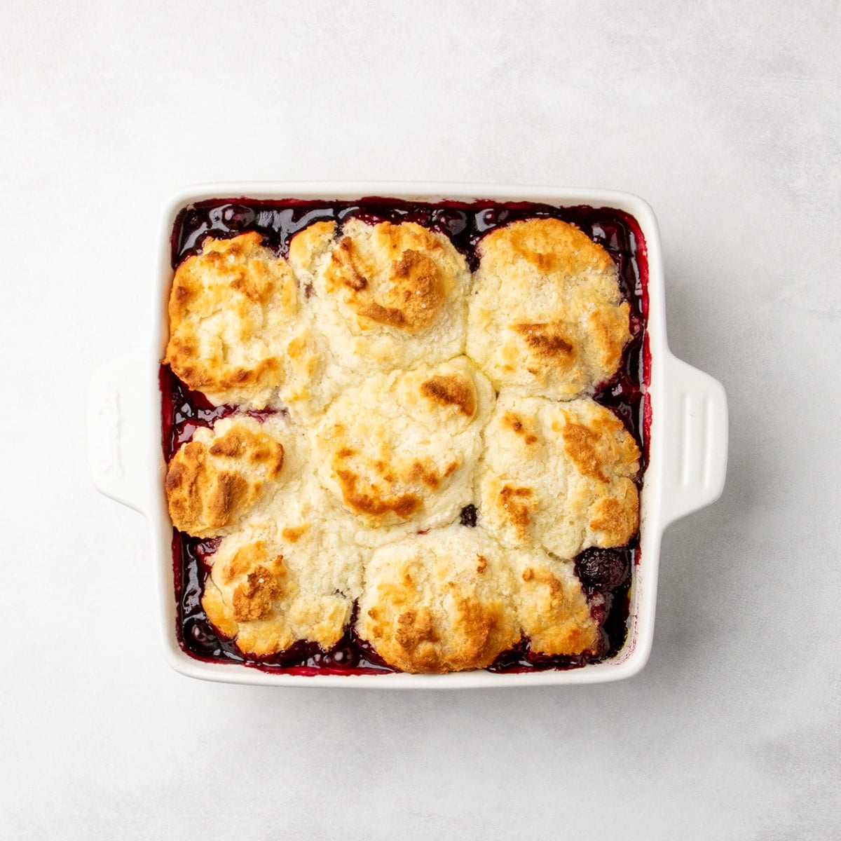 baked cobbler with golden brown topping and bubbling hot dark berry filling visible around the edges
