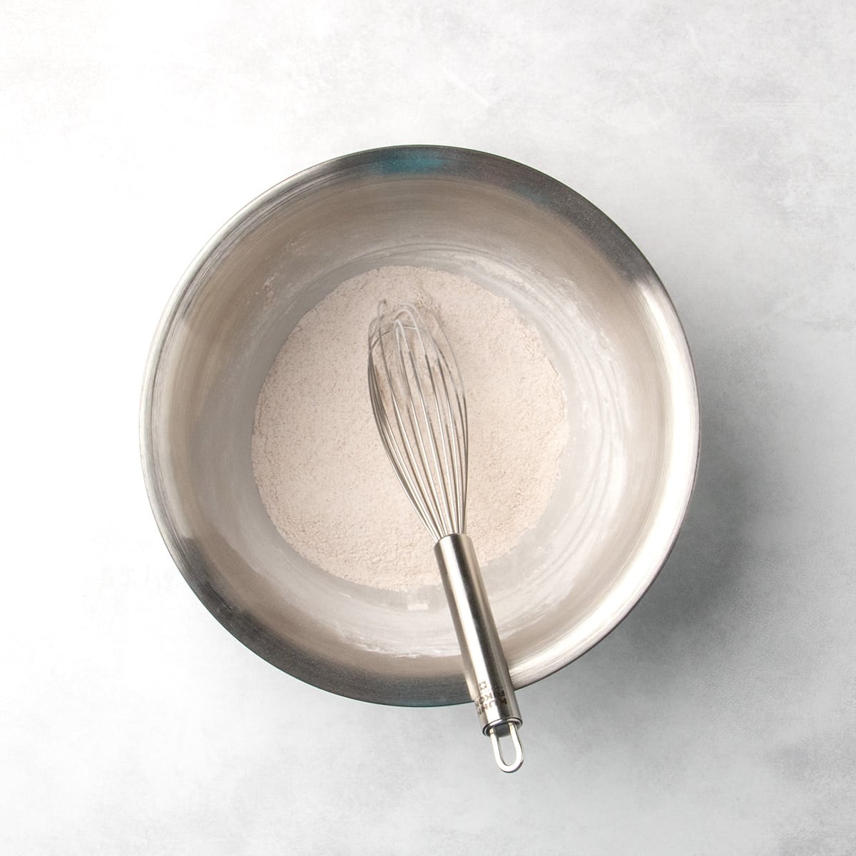 whisk resting inside a metal bowl with blended dry ingredients