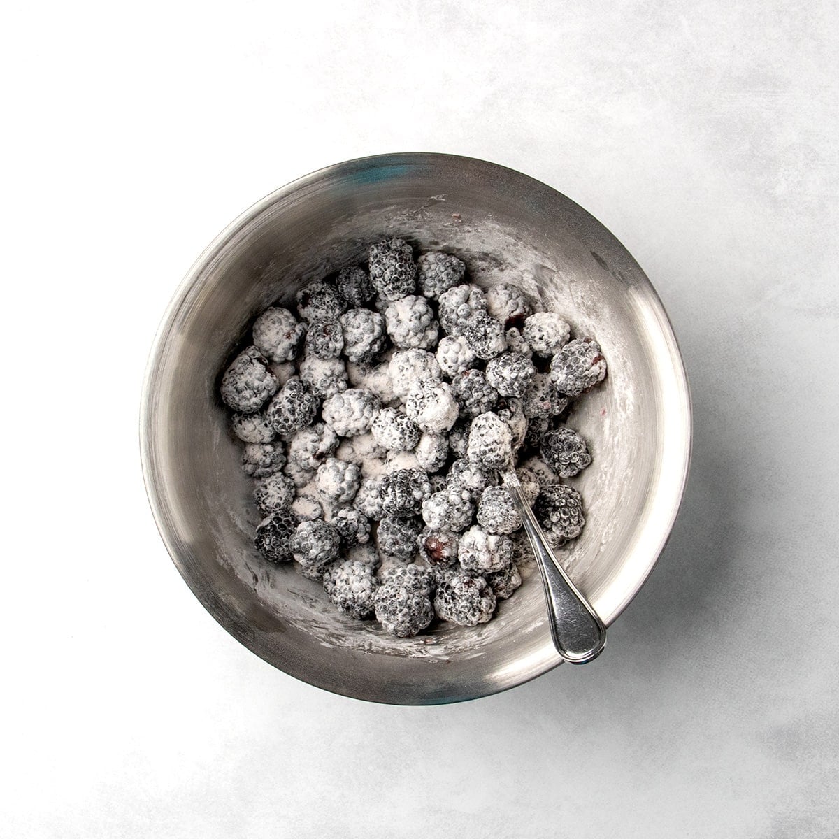 blackberries coated in a white powder mixture in a metal mixing bowl with a spoon