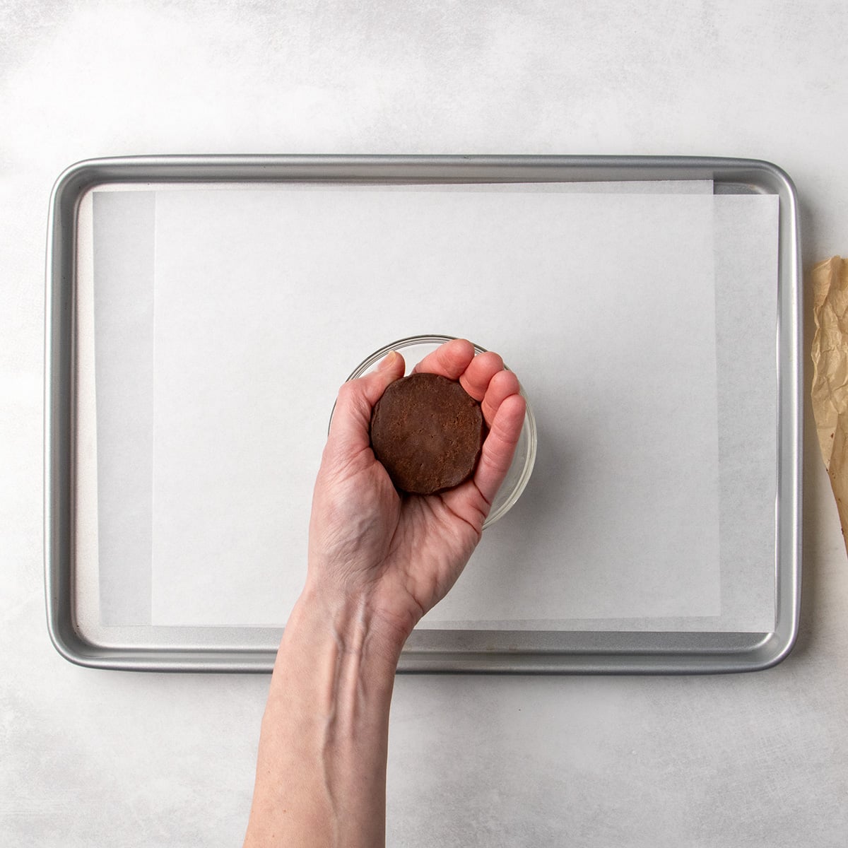 Hand holding a flattened round of chocolate dough over a parchment-lined baking sheet, trying to shape it into a cohesive round.