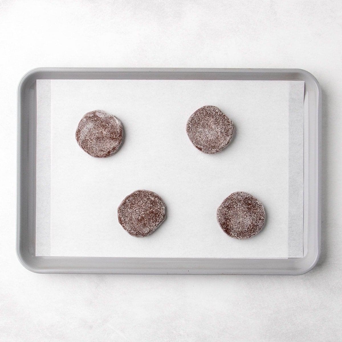 Four sugar-coated rounds of chocolate dough spaced about 2 1/2 inches apart on a parchment-lined baking sheet.