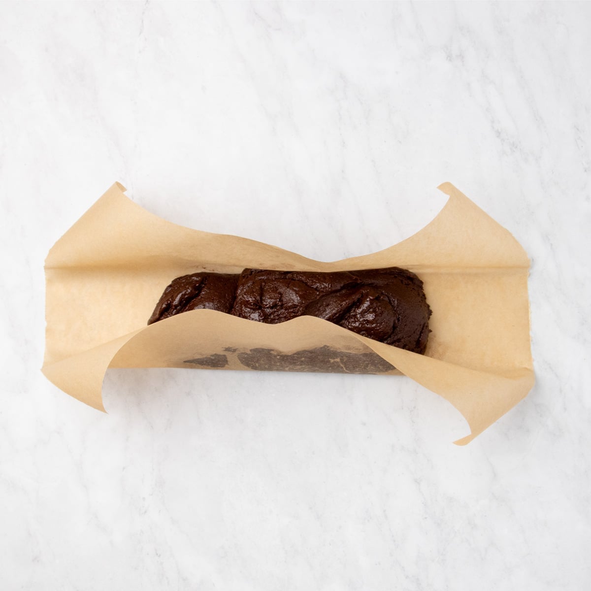 Raw, loosely unshaped chocolate dough placed on a rectangular sheet of brown parchment paper.