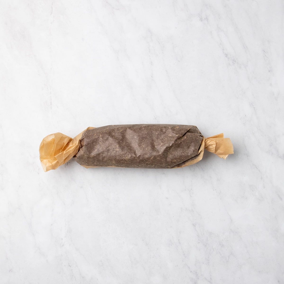 Raw chocolate cookie dough wrapped in parchment paper into a log shape with twisted ends.