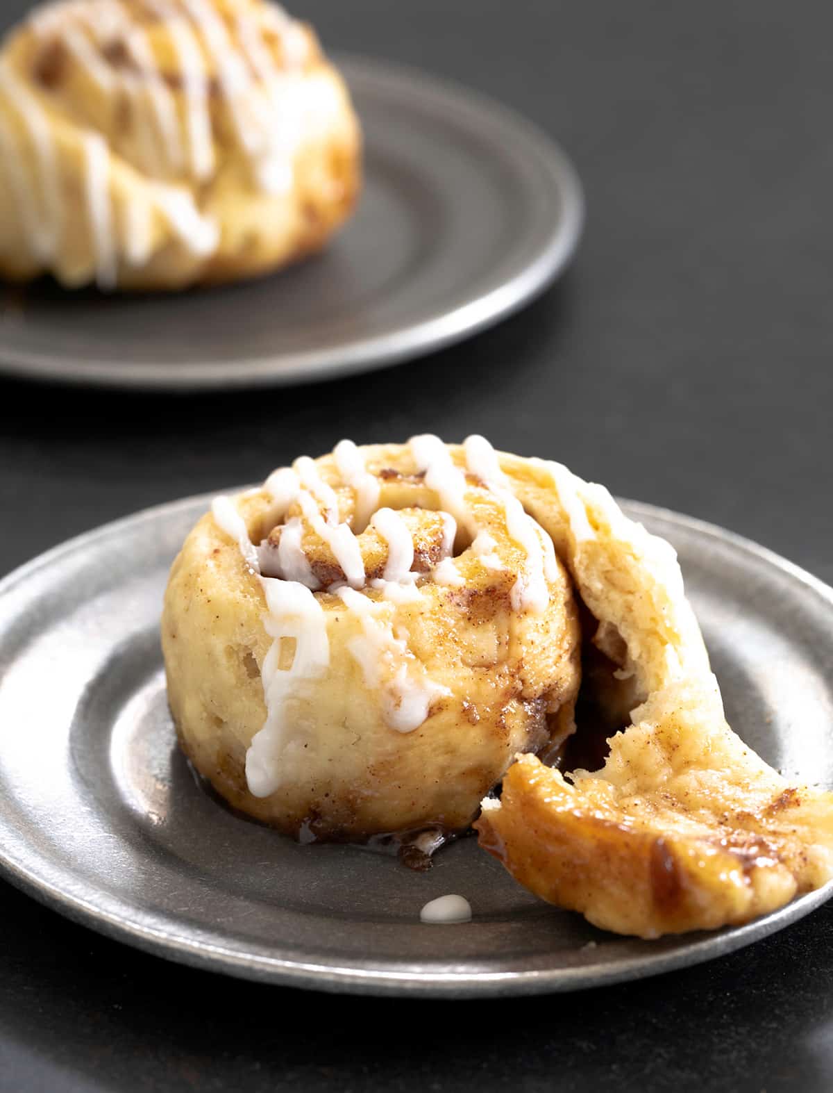 Cinnamon roll with melted brown sugar and drizzled white icing on a small plate.