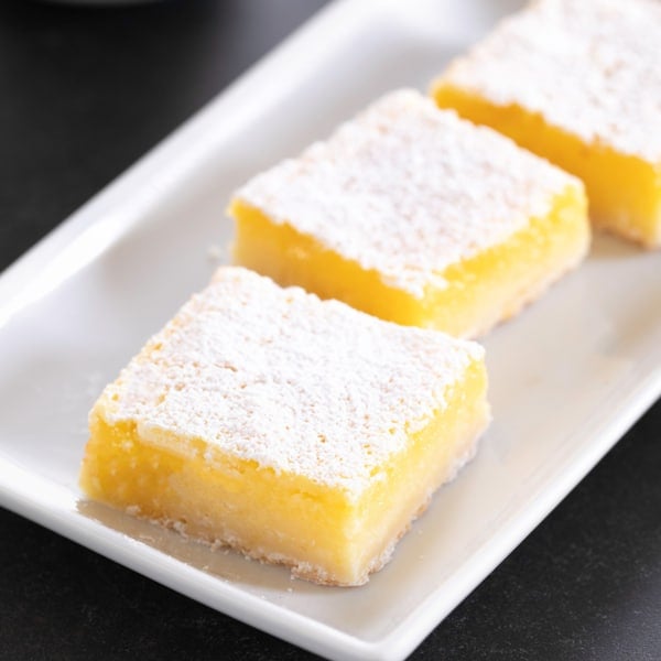 3 bright yellow gluten free lemon bars with powdered sugar on top on a rectangular white platter