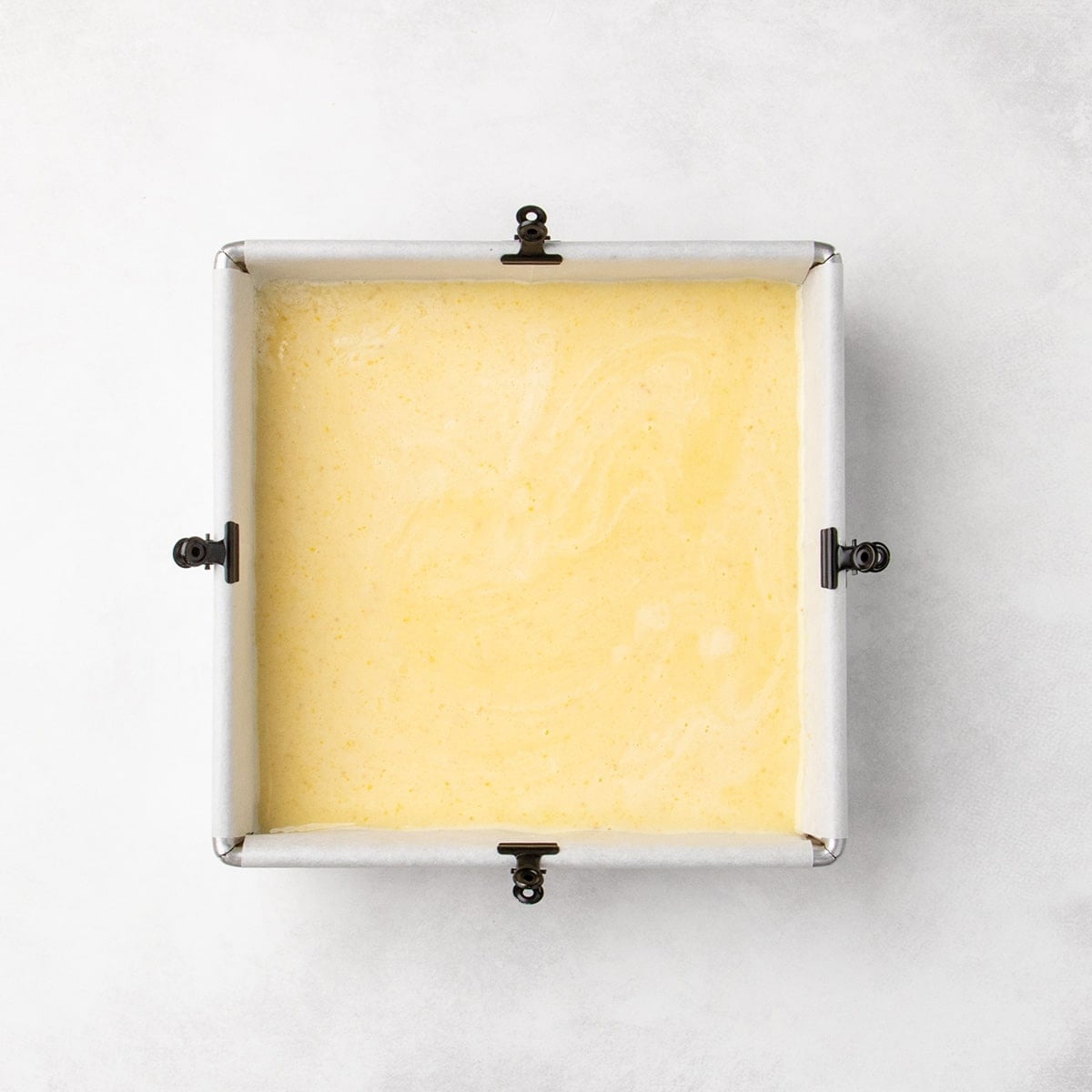 Square pan filled with a smooth pale yellow layer over the crust, spread evenly to the edges.