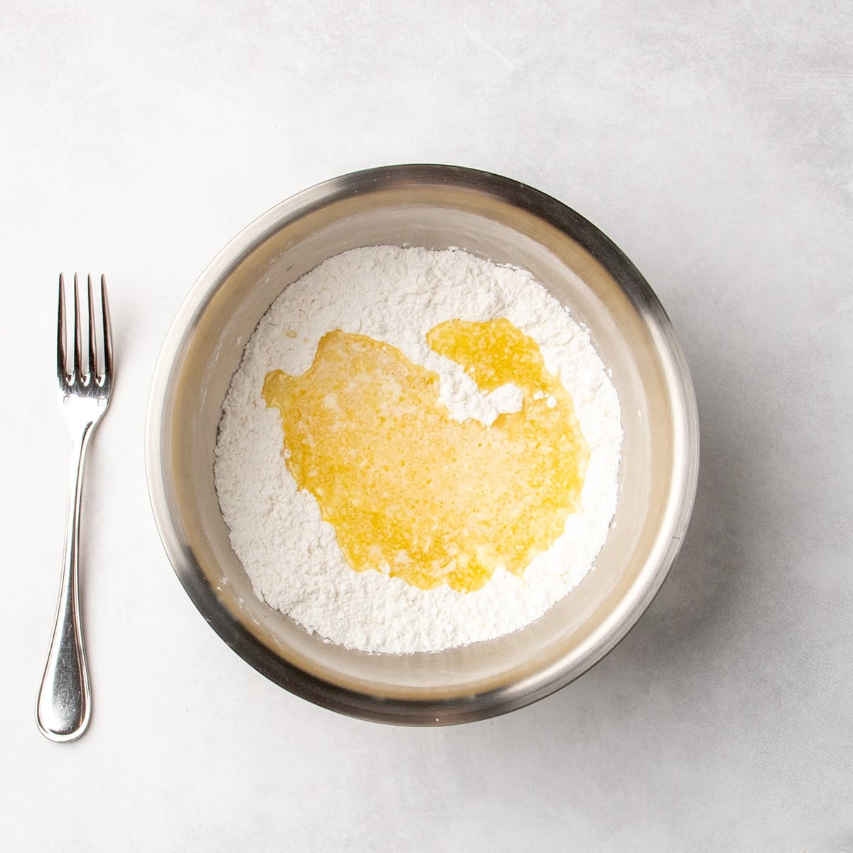 Melted butter mixture poured over white dry ingredients in a metal mixing bowl.