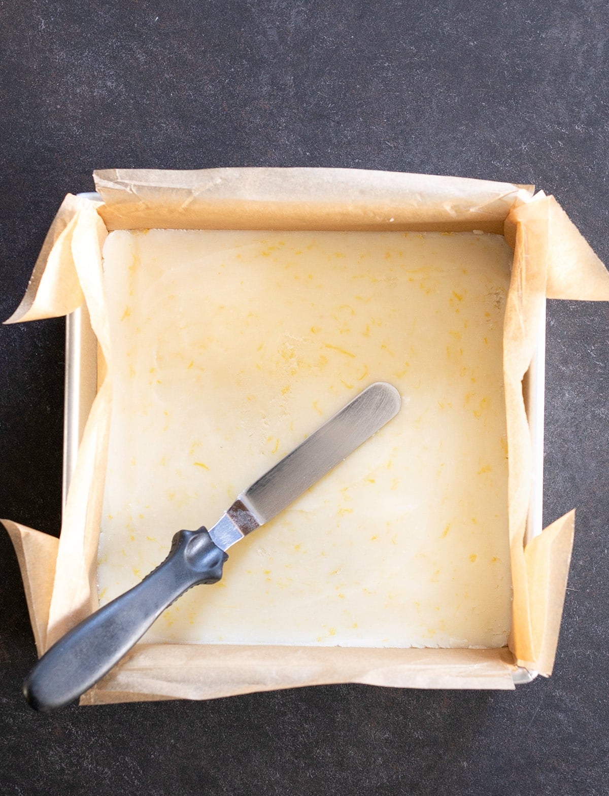 Overhead image of a square baking pan with raw crust and a spatula