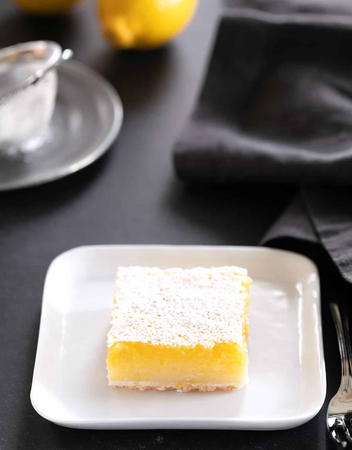 A single lemon bar on a small square plate