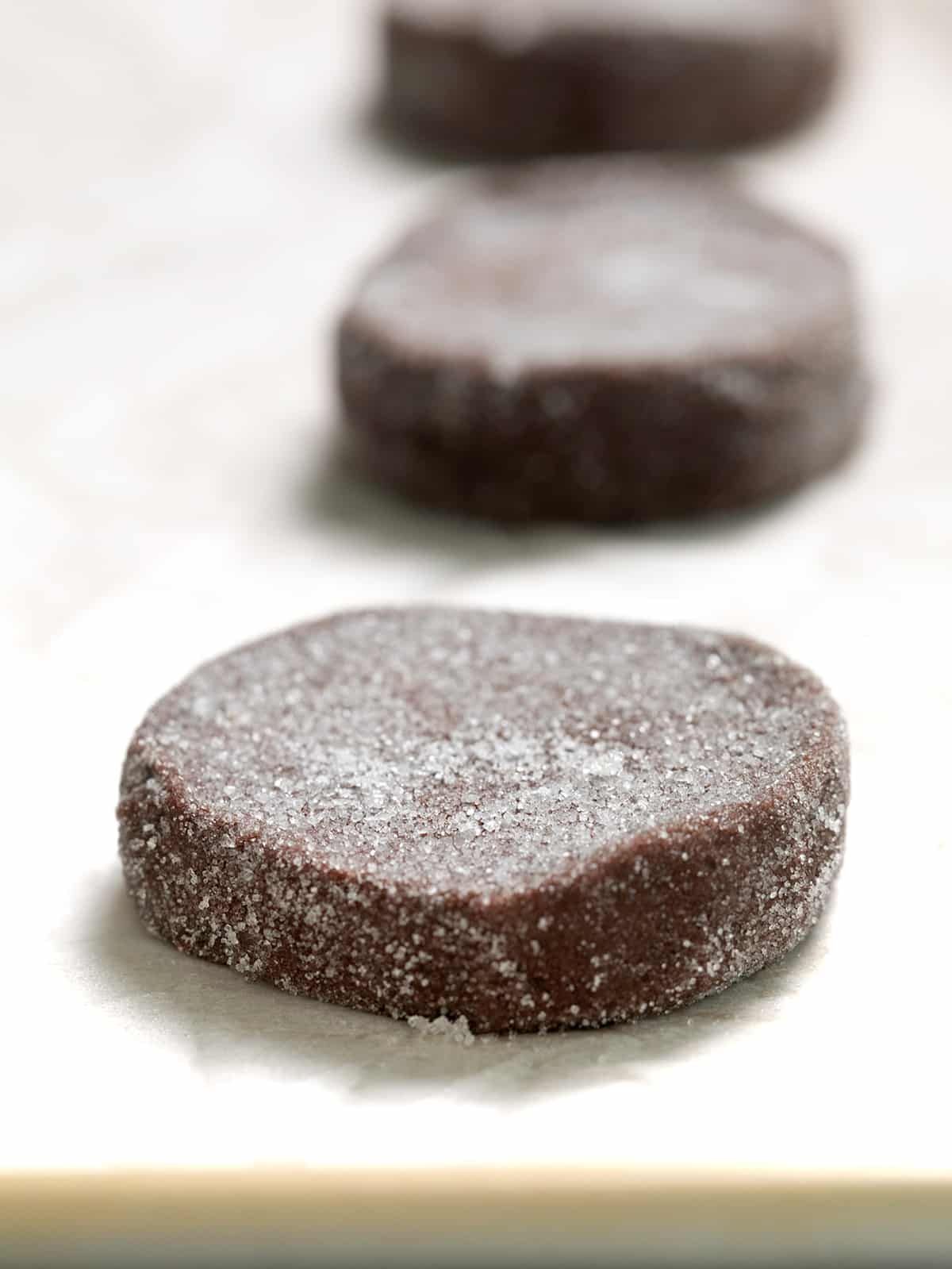 Raw shaped chocolate cookie dough with sugar coating on white paper