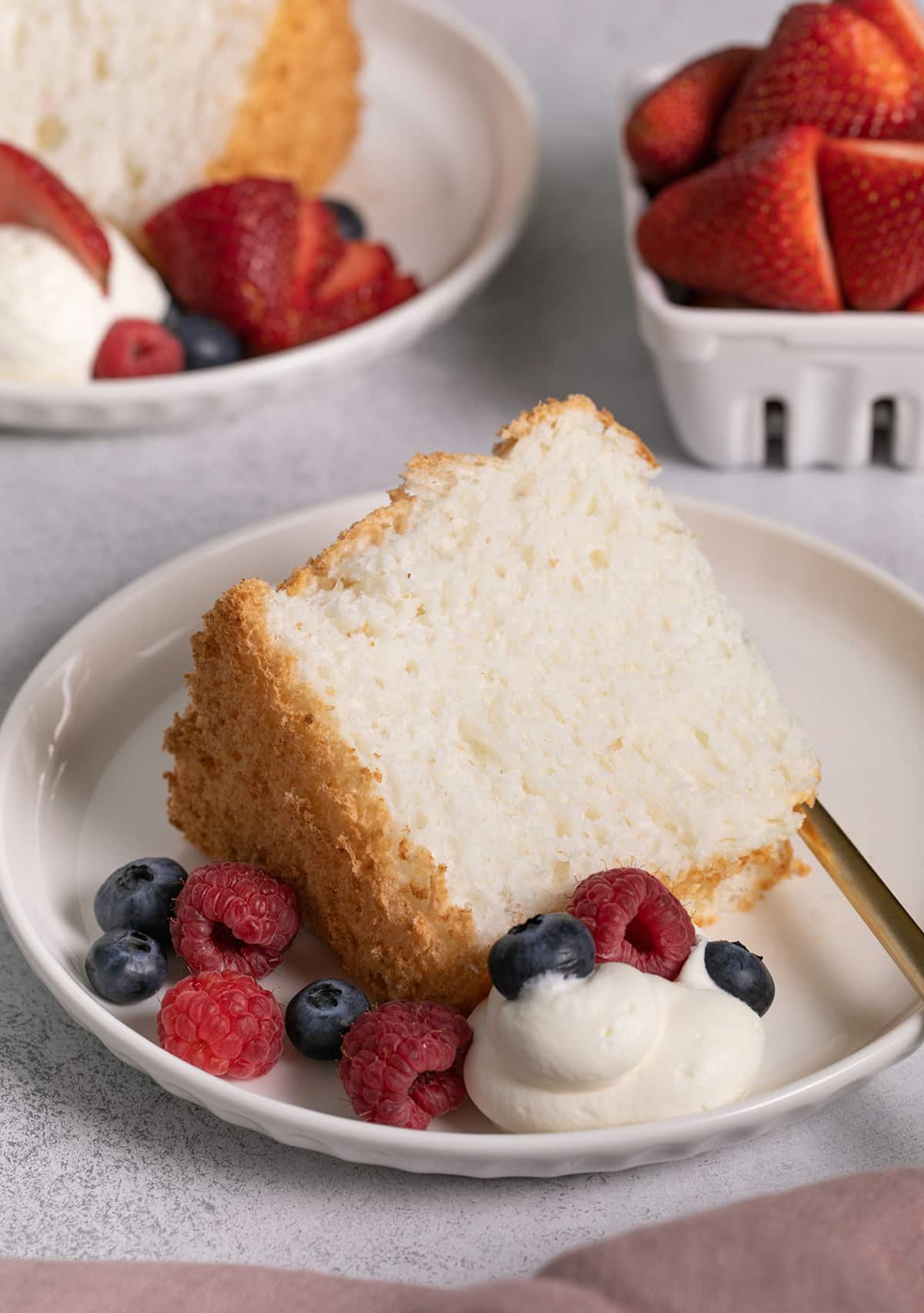 gluten free angel food cake on two small plates with whipped cream and berries