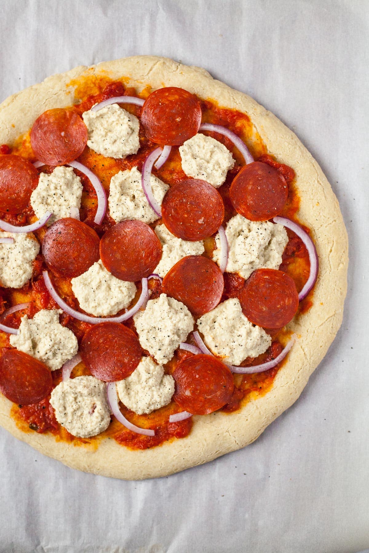 round baked pizza crust with unbaked dairy free cheese, pepperoni rounds and sliced onion toppings