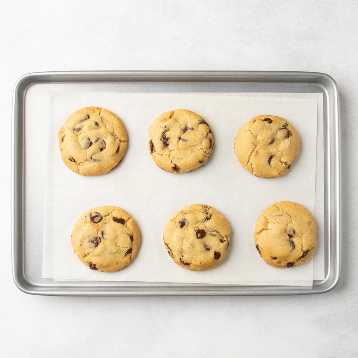 Same 6 rounds of dough now baked into perfect golden brown gluten free chocolate chip cookies on a parchment-lined baking sheet.