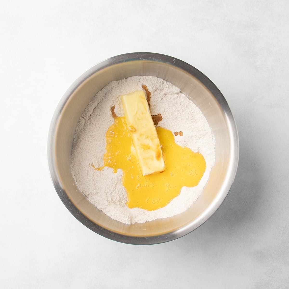 A softened stick of butter, a beaten egg, and vanilla extra on top of whisked dry ingredients in a metal mixing bowl.