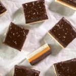 Chocolate-topped gluten free caramel shortbread squares with coarse salt scattered on parchment paper.