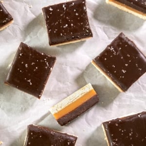 Chocolate-topped gluten free caramel shortbread squares with coarse salt scattered on parchment paper.