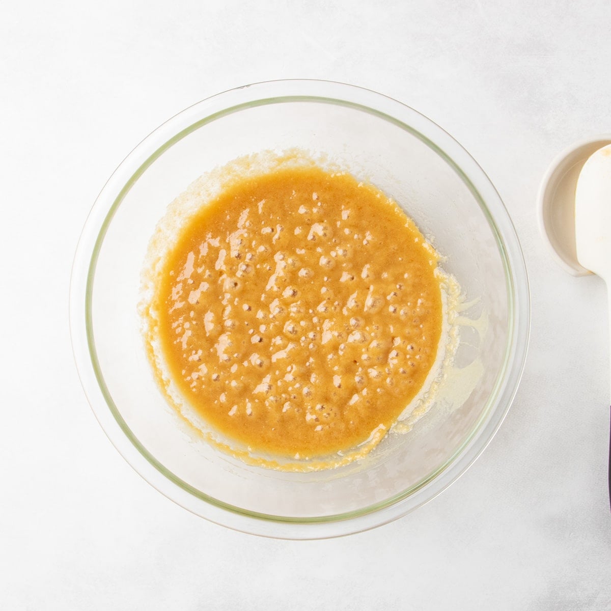 Bubbly caramel-colored mixture in a clear glass mixing bowl.