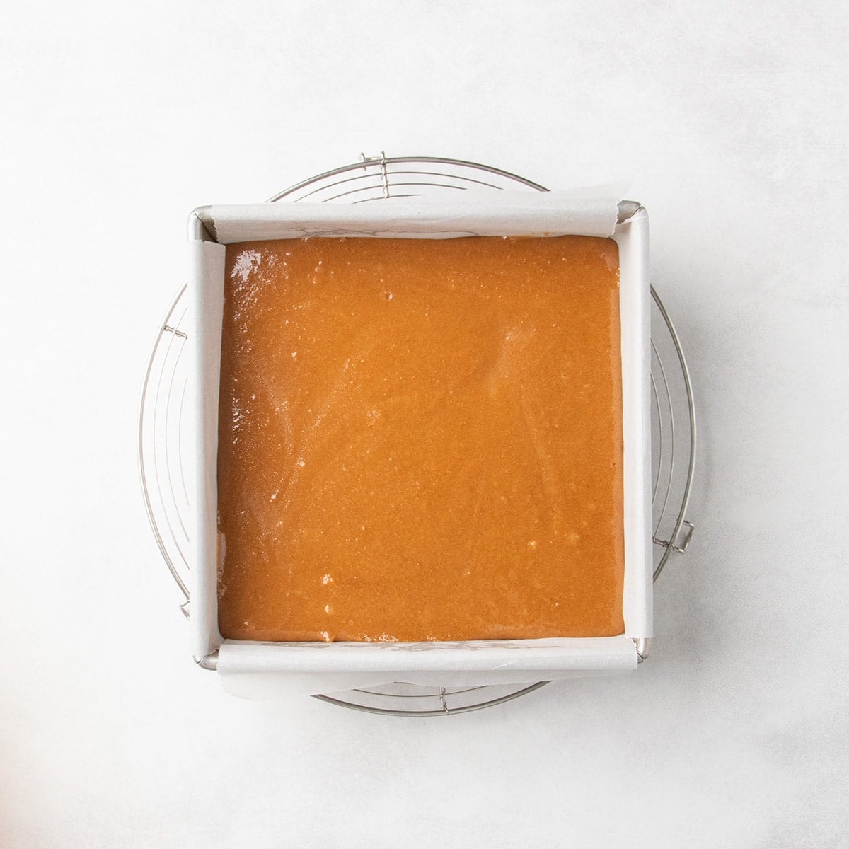 Smooth caramel layer spread in an even layer in a parchment-lined square pan on a wire cooling rack.