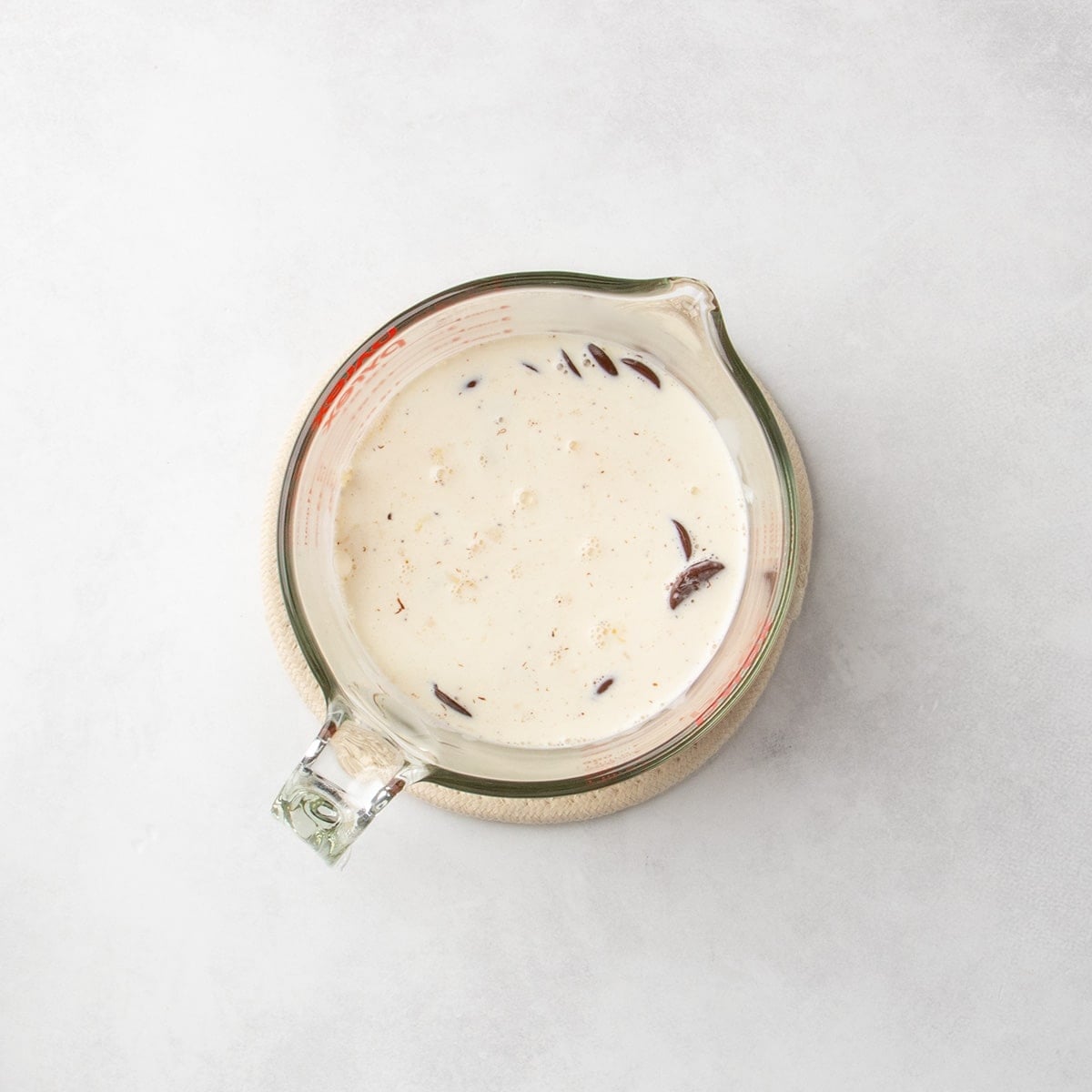 Chocolate pieces partly covered with cream in a glass measuring cup.
