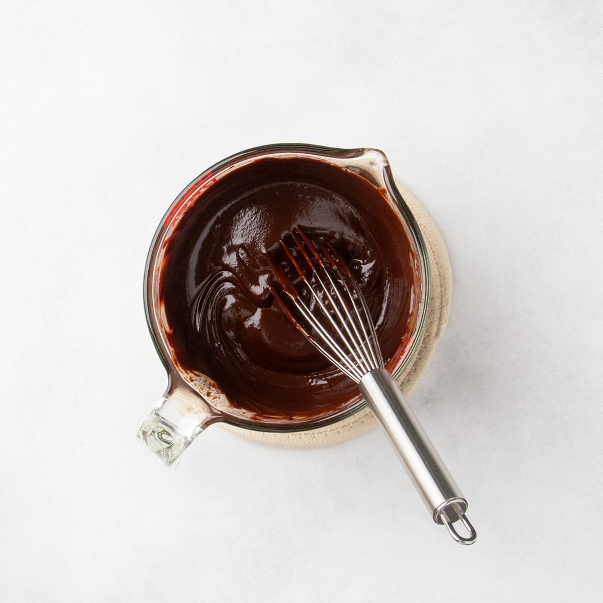 Smooth melted chocolate mixture in a glass measuring cup with a whisk inside.