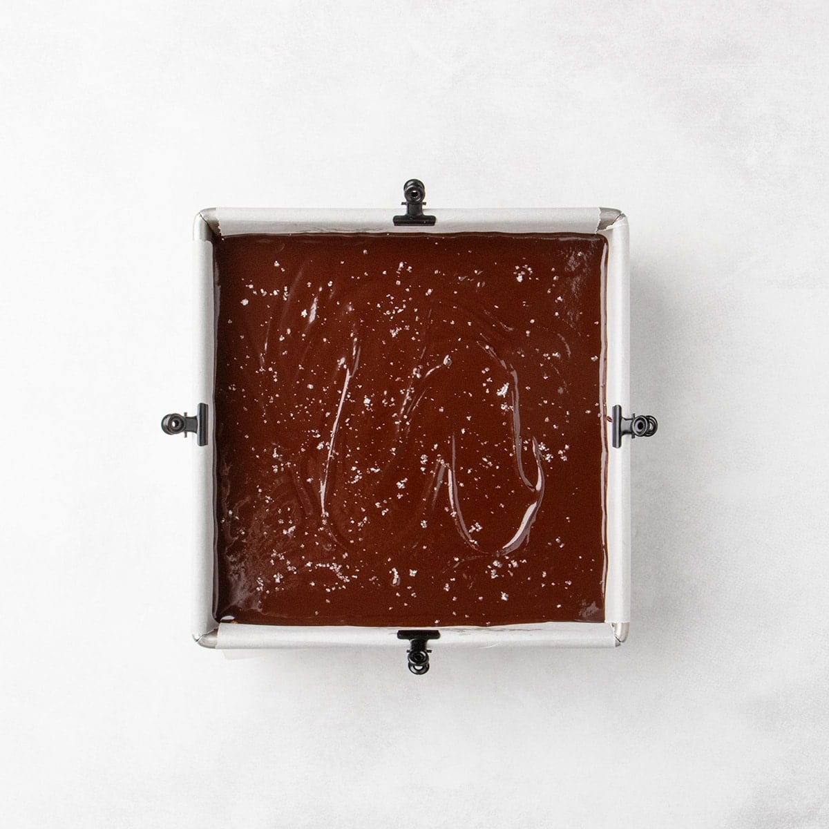 Glossy chocolate layer with coarse salt in a parchment-lined square pan.
