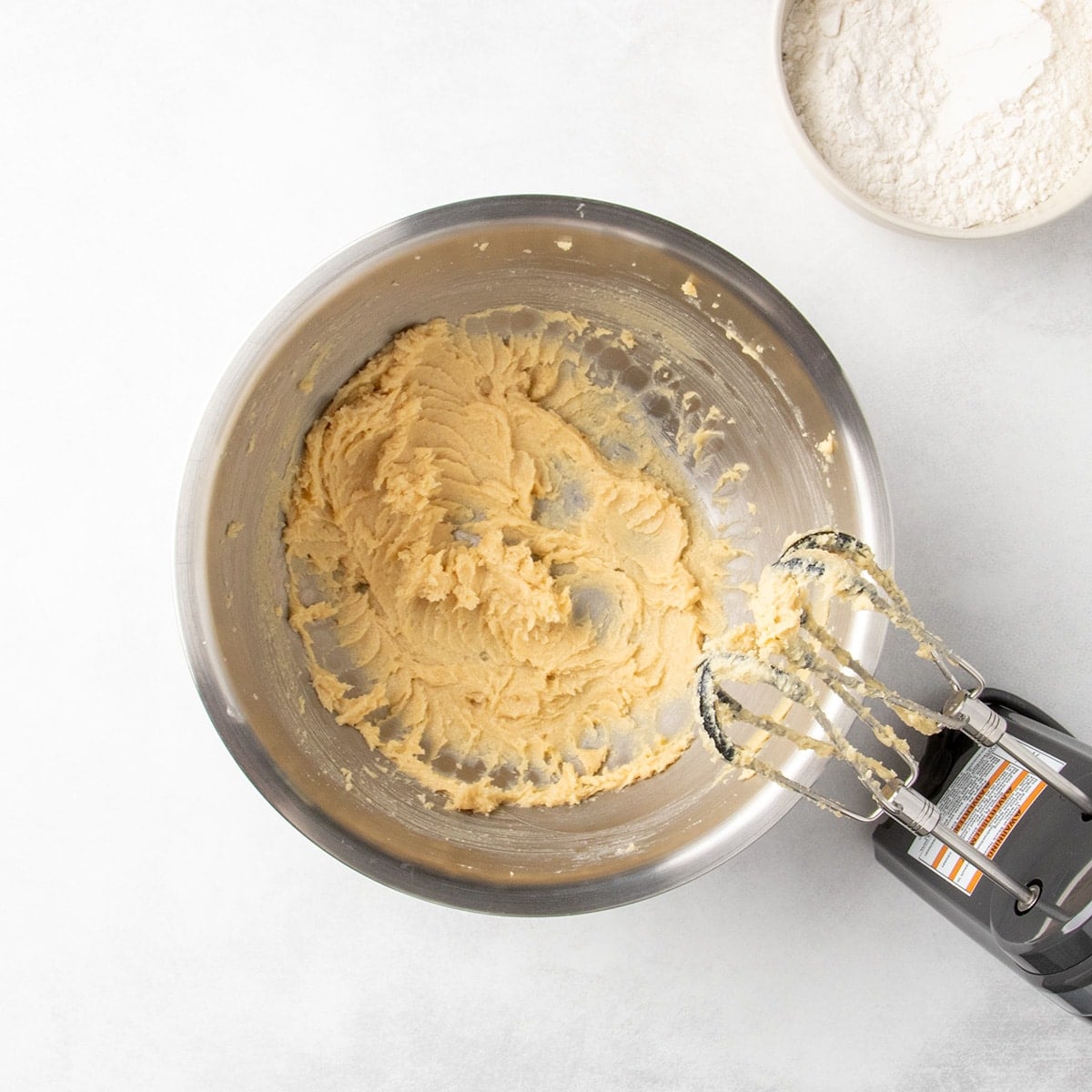 Creamed butter and sugar in a metal mixing bowl with a hand mixer resting on the side.