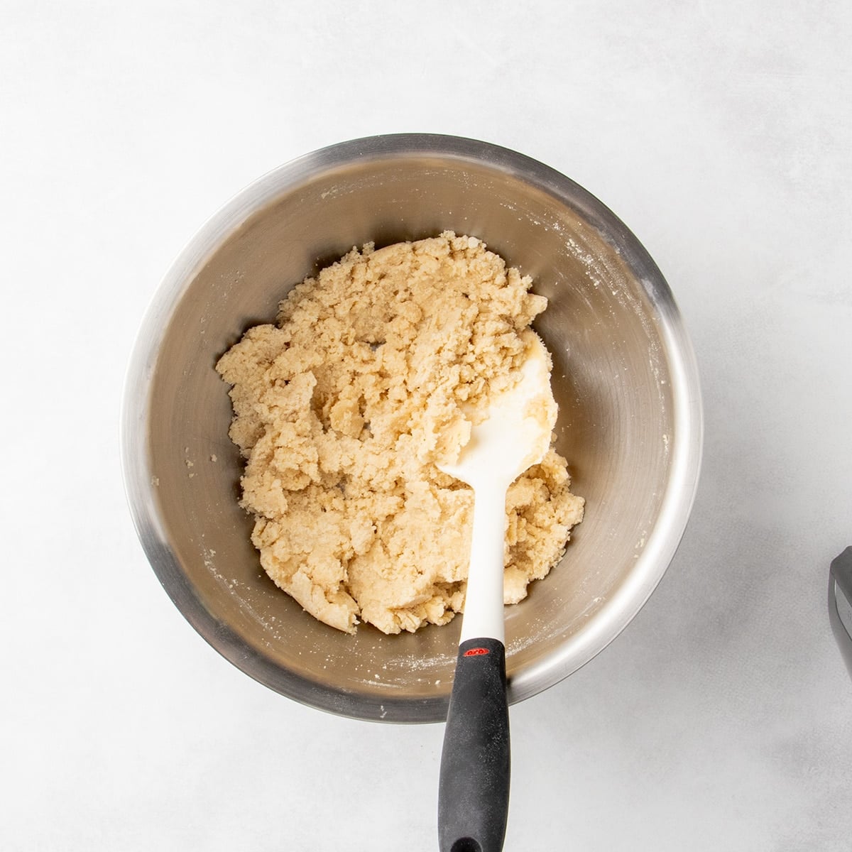 Raw light brown dough in a metal mixing bowl with a white spatula resting on top.