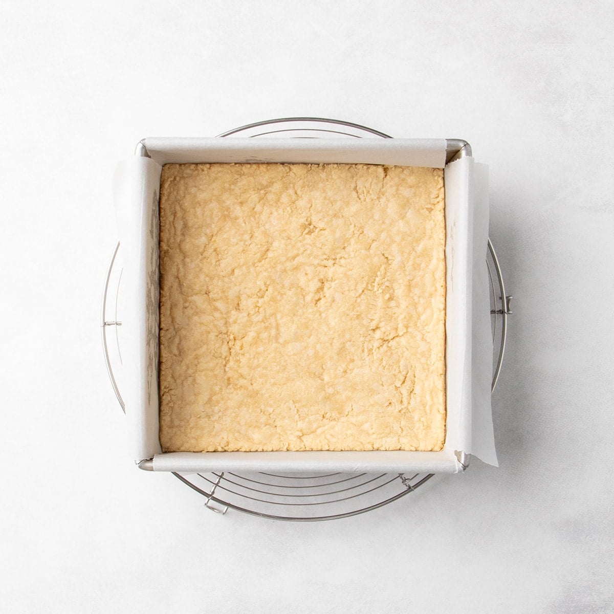 Baked shortbread in a parchment-lined square pan set on a wire cooling rack.