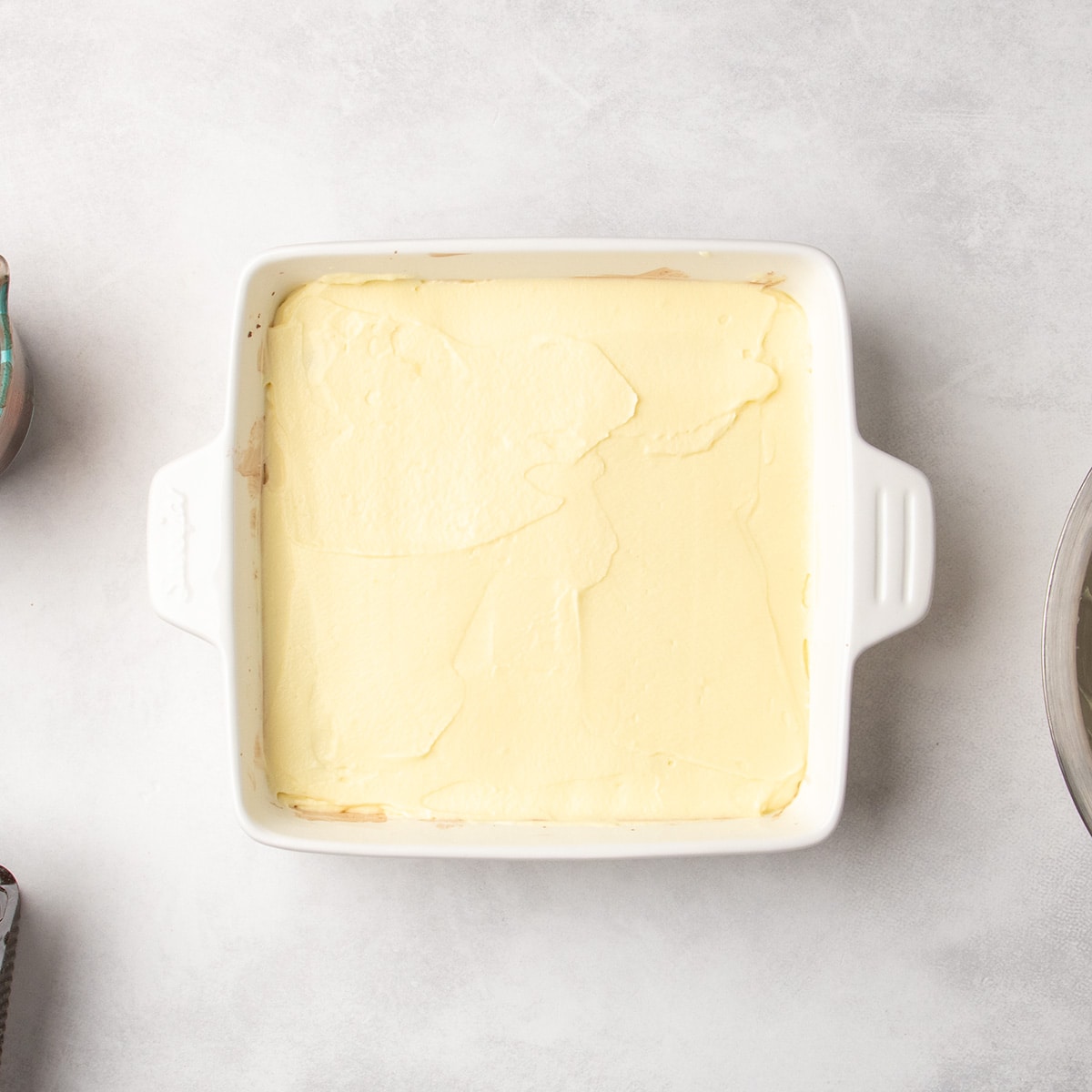 White baking dish filled with a smooth pale yellow layer spread over cookies, cookies no longer visible.