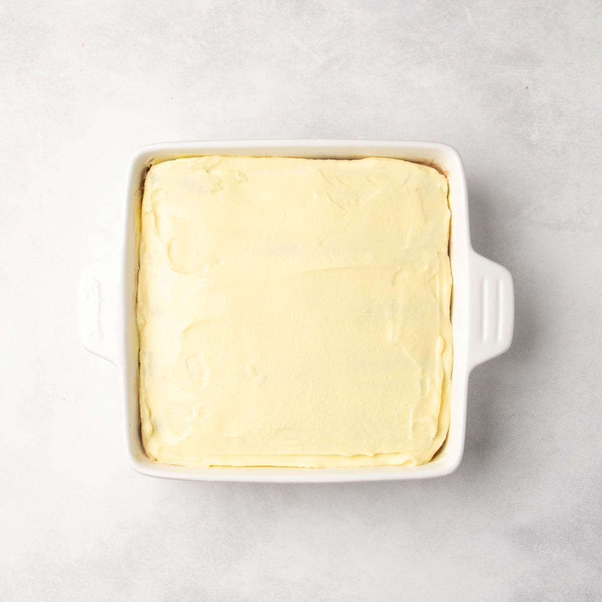 White baking dish filled with a smooth pale yellow layer.