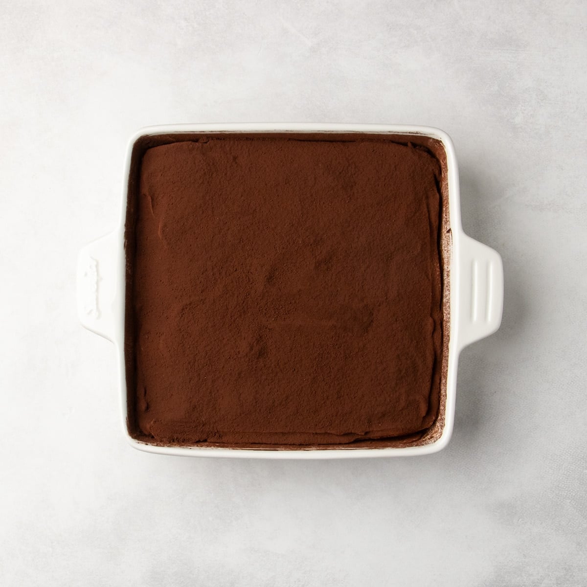 White baking dish filled with a smooth dark brown powdered layer of cocoa powder.