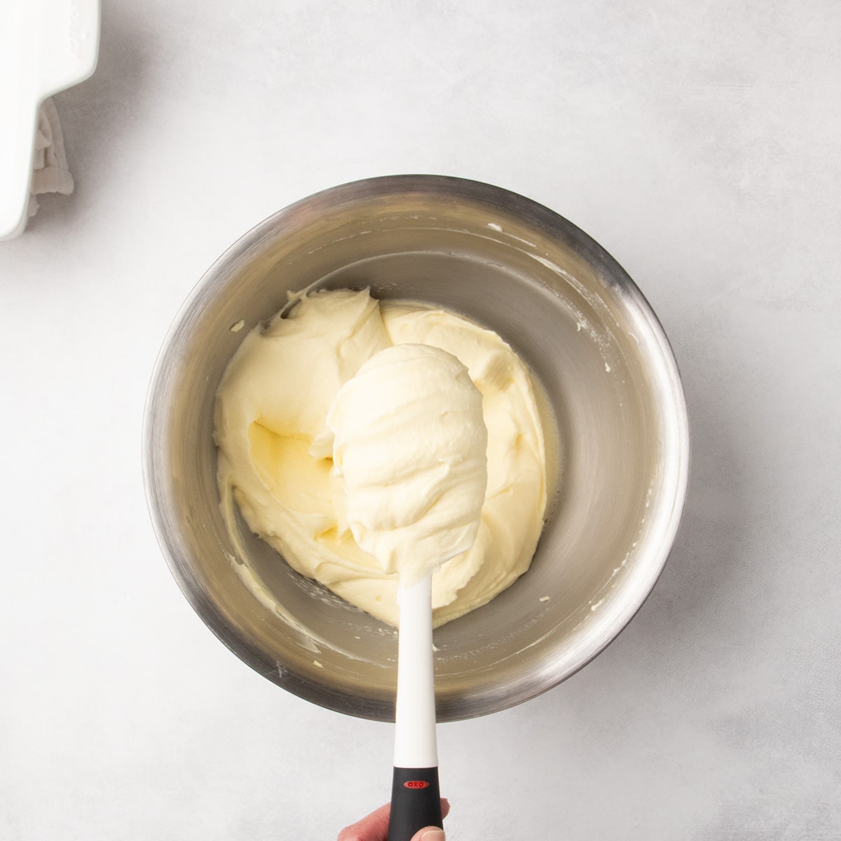 Smooth pale yellow mixture in a metal bowl with a white spatula lifted above it.