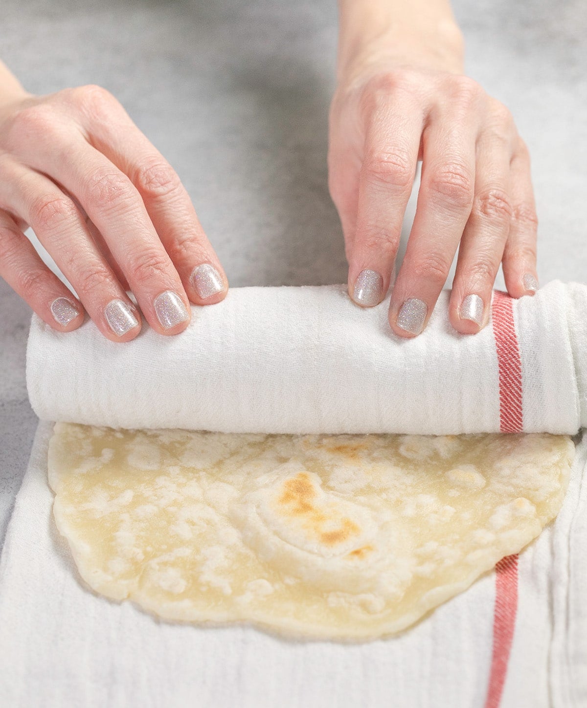 Hands rolling flatbread in a white towel with a red stripe