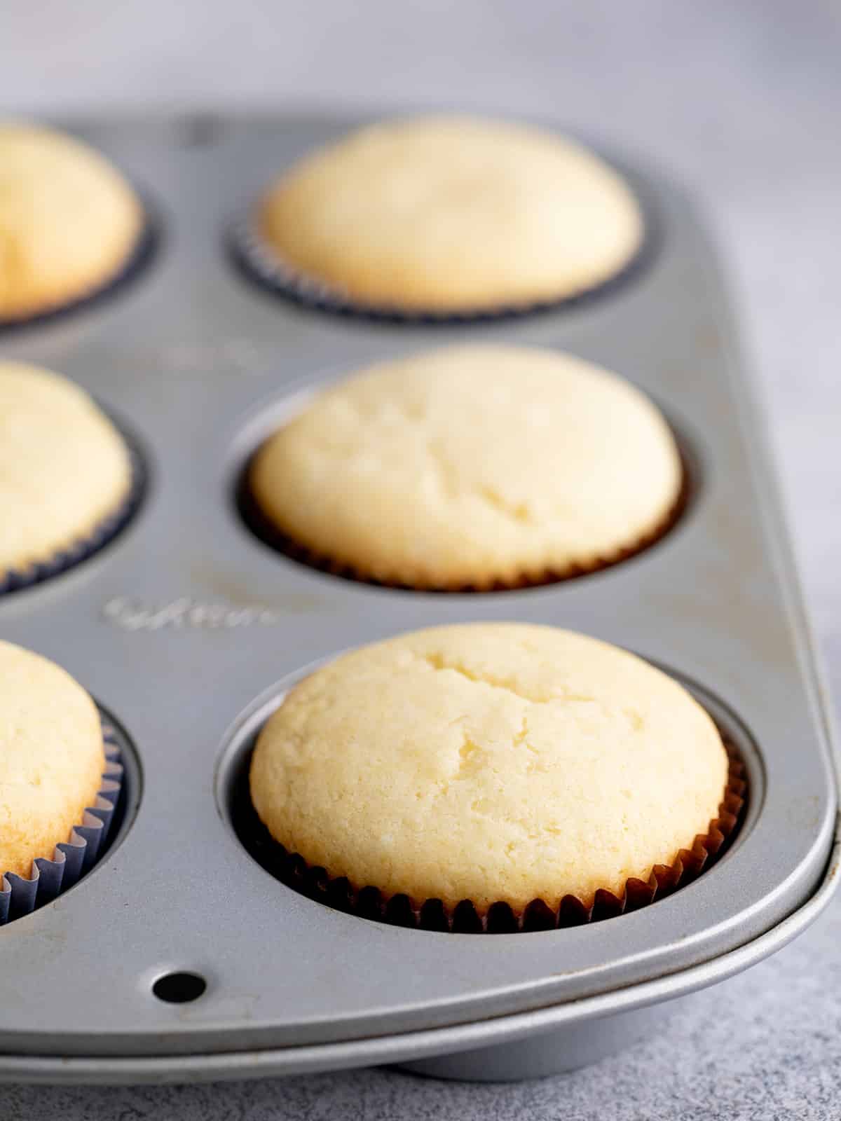Baked gluten free vanilla cupcakes in 6 well cupcake tin in brown liners on purple cloth