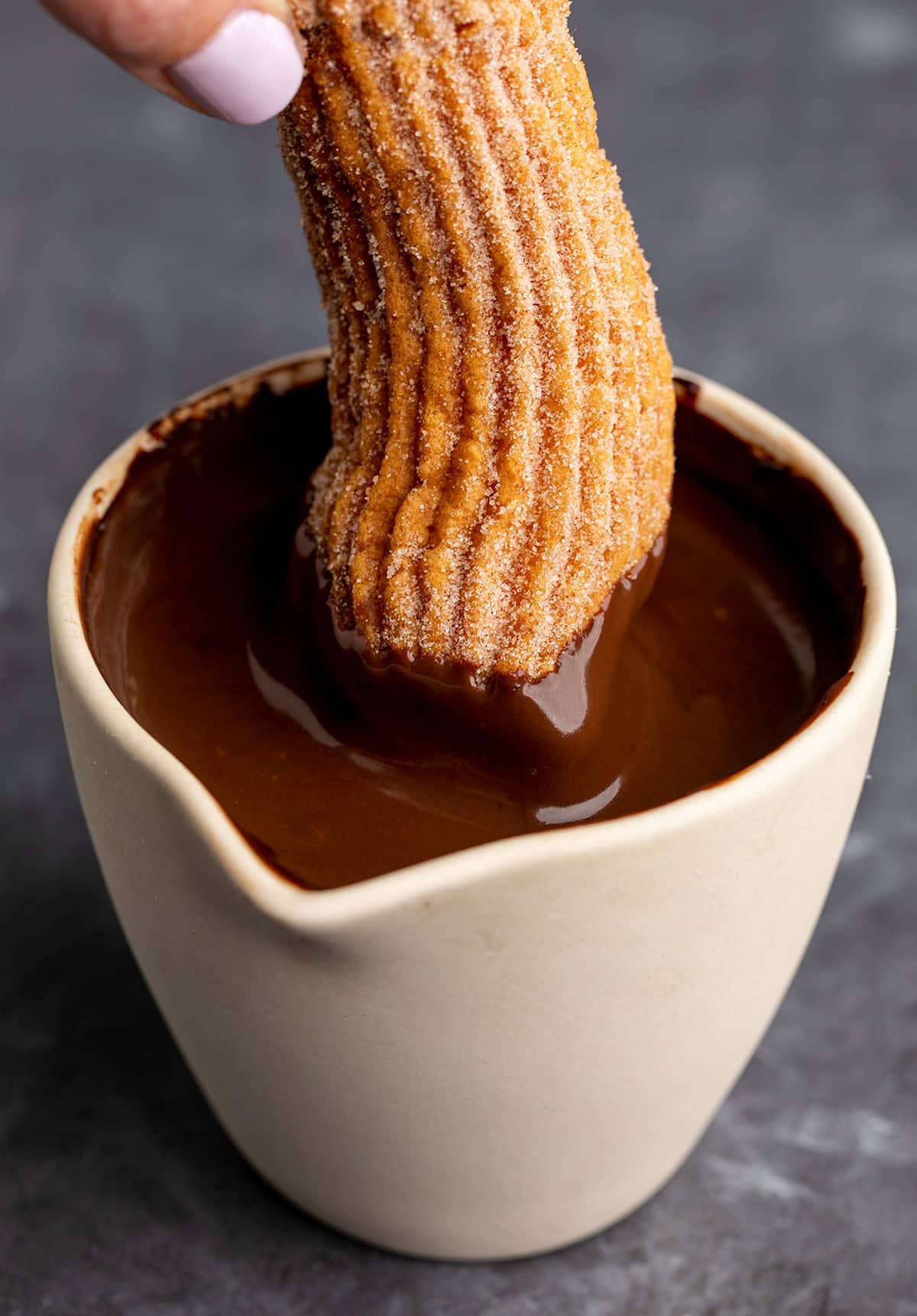 Fingers holding churro dipping into chocolate sauce in jar