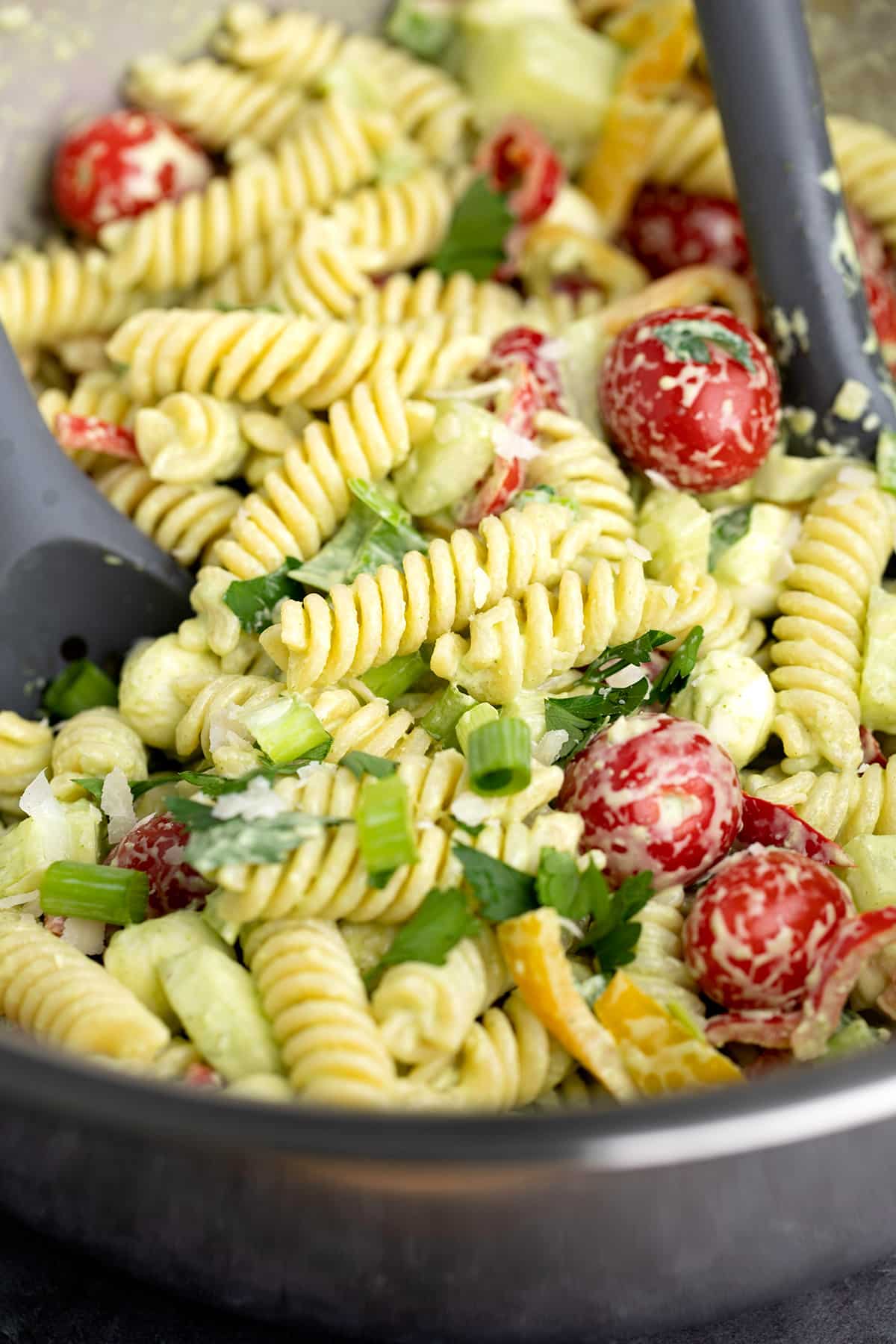 Fusilli tomatoes scallions and green goddess dressing in metal bowl with black serving spoons