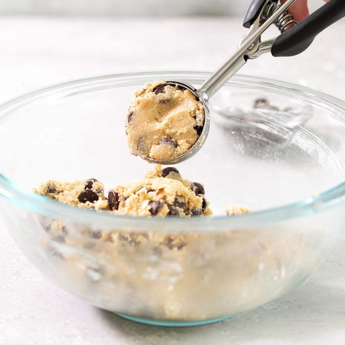 same glass bowl with cookie scoop portioning a single scoop of raw cookie dough