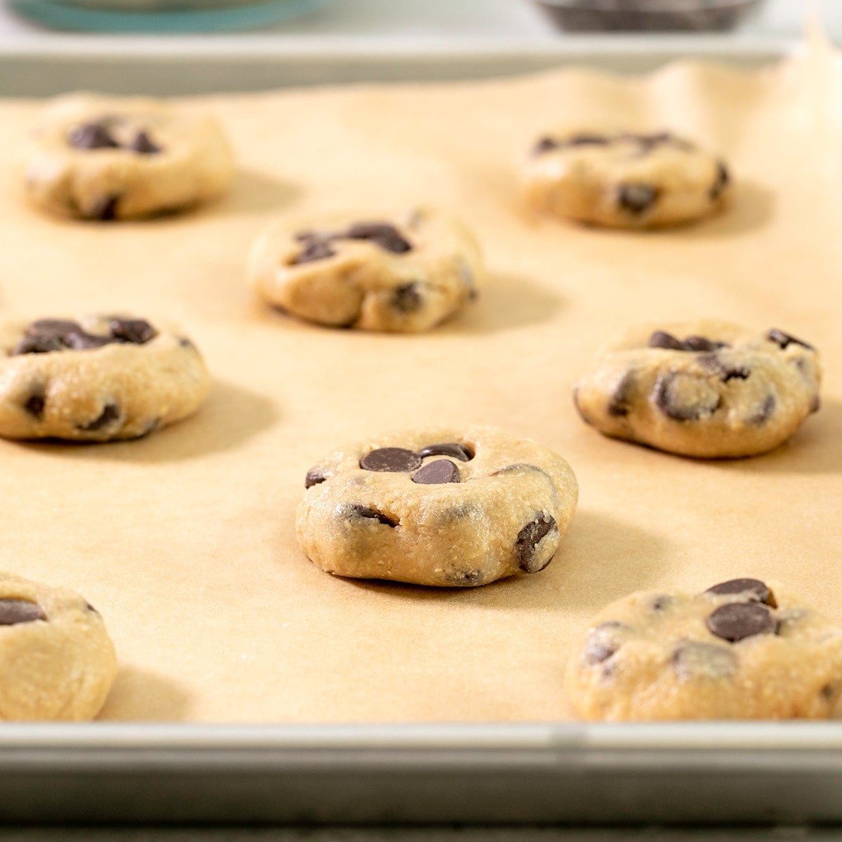 raw disks of chocolate chip cookie dough on a parchment lined baking sheet