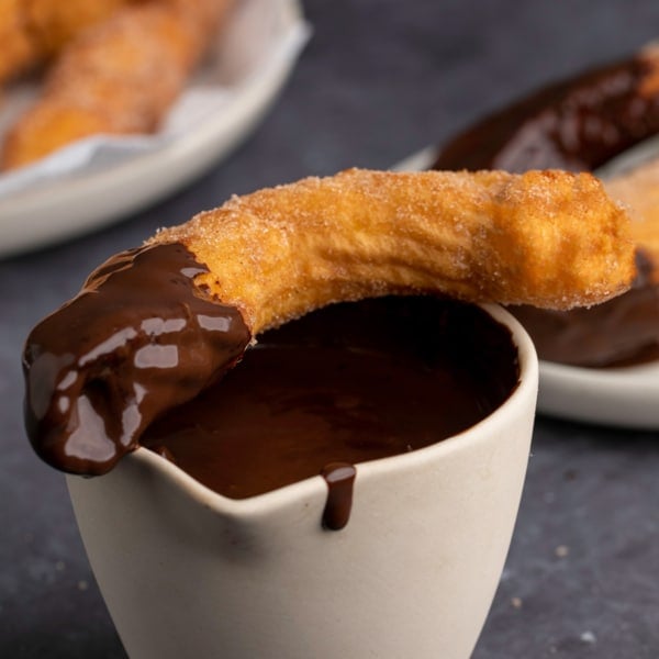 closeup image of gluten free churro dipped in chocolate sauce sitting on top of rest of sauce