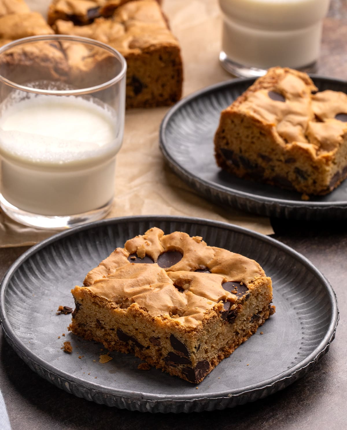 Chocolate chip gluten free cookie bar on a round dark gray plate with a glass of milk and more cookie bars in the background.